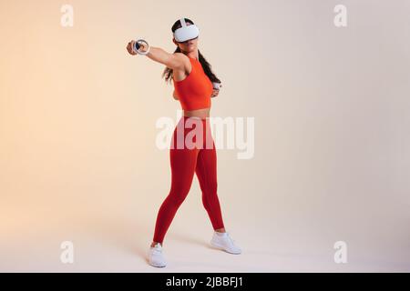 Frau, die eine Boxsitzung in der virtuellen Realität hat. Aktive junge Frau, die ein Fitnessspiel mit Gaming-Controllern spielt. Athletische junge Frau, die ein vi trägt Stockfoto