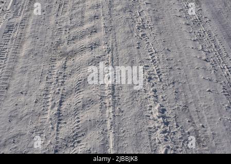 Eine winterlich mit Schnee bedeckte Straße, die Reifenspuren im Sonnenlicht zeigt Stockfoto