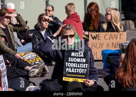 Missä Suomen todelliset päästöt? Sitzende Frau mit einem Plakat auf Elokapinas Straßenblockierungsdemonstration in Mannerheimintie, Helsinki, Finnland. Stockfoto