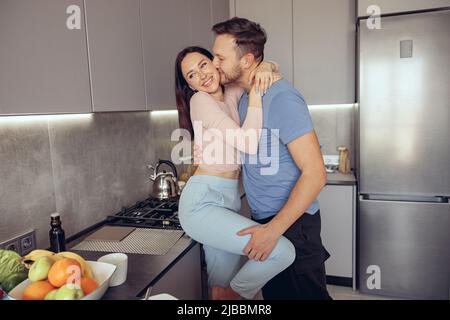 Kaukasisch schöner Mann küsst schöne Frau, während Paar in der Küche stehen. Stockfoto