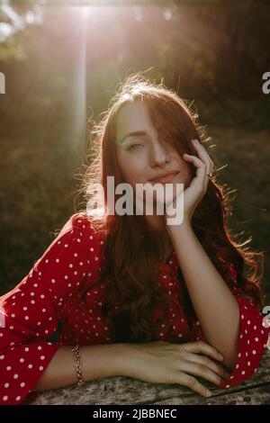 Nahaufnahme Gesicht Portrait Schönheit kaukasische weiße Frau mit roten langen lockigen Haaren in rotem Hemd gekleidet, den Kopf von Hand haltend und Blick auf die Kamera Stockfoto