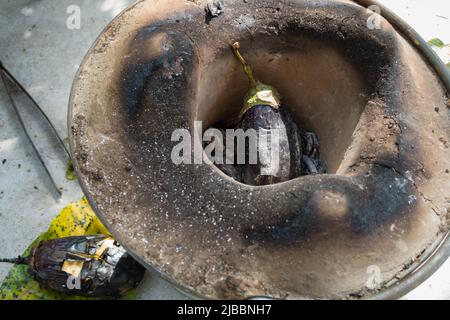 Ganze geröstete Aubergine oder Brinjal in einem traditionellen Ton Angeethi oder Kamin in Nordindien. Stockfoto