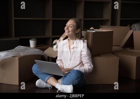 Junge attraktive Frau verwenden Laptop, um am Umzugstag Ordnung zu machen Stockfoto