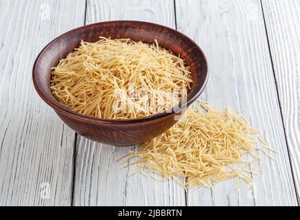 Ungekochte Vermicelli Pasta in Keramikschale auf weißem Holzhintergrund Stockfoto