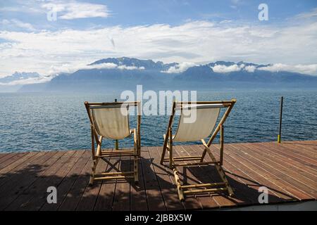 Zwei Liegestühle auf einem hölzernen Ponton vor einem ruhigen See Stockfoto