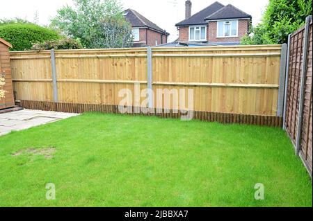 Ein Gartenzaun in Großbritannien mit einem kleinen Pfostenzaun, der Korbbretter versteckt. Stockfoto