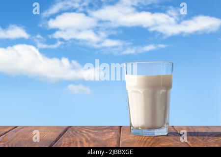 Milch im Glas auf dem Tisch mit blauem Himmel und Wolken auf dem Hintergrund Stockfoto