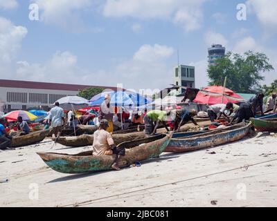 Dar es Salaam, Tansania - Februar 2021: Das tägliche Leben afrikanischer Fischer auf dem Kivukoni Fischmarkt. Befestigung von Holzkanus und Entwirren der Netze. Co Stockfoto