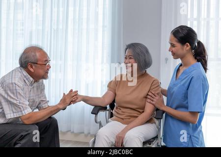 Junge Krankenschwester kümmert sich um ältere behinderte Frau, die im Rollstuhl mit Kopierraum sitzt. Eine weibliche Unterstützerin, die einer älteren Patientin hilft, während sie lächelt Stockfoto