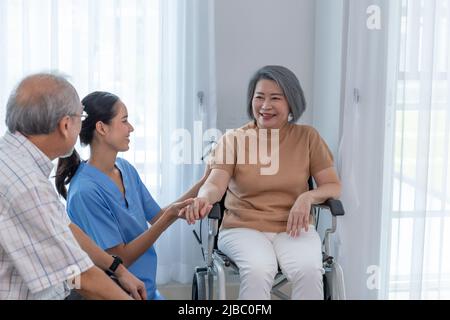 Junge Krankenschwester kümmert sich um ältere behinderte Frau, die im Rollstuhl mit Kopierraum sitzt. Eine weibliche Unterstützerin, die einer älteren Patientin hilft, während sie lächelt Stockfoto