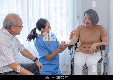 Junge Krankenschwester kümmert sich um ältere behinderte Frau, die im Rollstuhl mit Kopierraum sitzt. Eine weibliche Unterstützerin, die einer älteren Patientin hilft, während sie lächelt Stockfoto