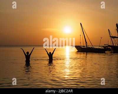 Kizimkazi, Sansibar - Jan, 2021: Traditionelle Dhow-Boote und Menschen, die während der Sonnenuntergangszeit im Indischen Ozean baden., Sansibar, Tansania, Afrika Stockfoto