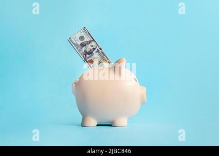 Sparschwein. Das Konzept der Erhaltung und des Sparens von Geld. Dollar im Sparschwein auf blauem Hintergrund. Seitenansicht Stockfoto