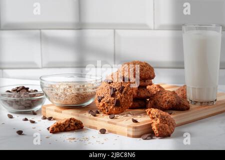 Hausgemachte Haferkekse mit Schokolade und einem Glas Milch. Gesundes Frühstück auf Holzbrett. Rustikaler Snack für einen gesunden Lebensstil. Stockfoto