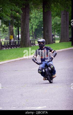 Ein junger Mann mit viel Schutzausrüstung fährt an einem milden späten Frühlingstag im Flushing Meadows Corona Park mit einem elektrischen Einrad. Stockfoto