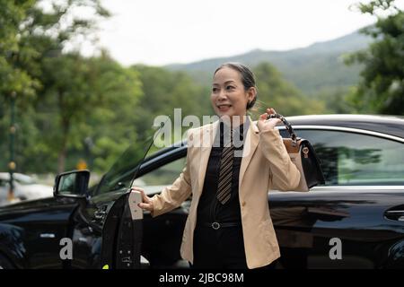 Asiatische reife Geschäft Erfolg Frau Ausstieg aus dem Luxusauto Stockfoto