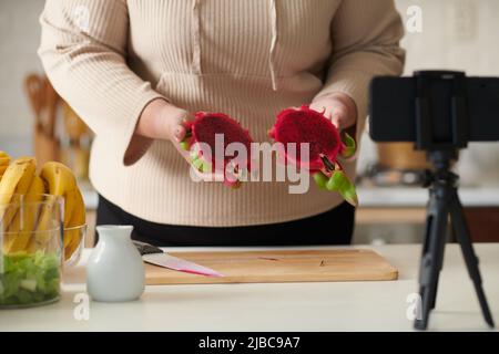 Zugeschnittenes Bild einer Frau in Übergröße, die sich beim Schneiden von Libellenfrüchten für ein gesundes Frühstücksgericht filmt Stockfoto