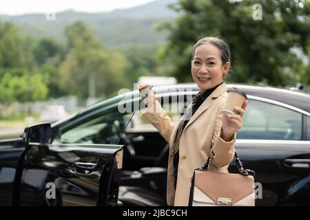 Selbstbewusste Geschäftsfrau, die mit lächelndem Blick auf die Kamera aus dem Luxuswagen steigt Stockfoto