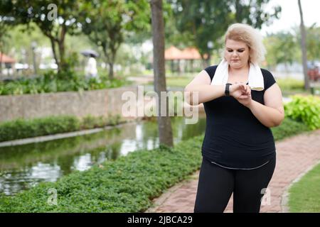 Plus Größe junge Frau Überprüfung Fitness-Tracker nach dem Laufen im Freien Stockfoto