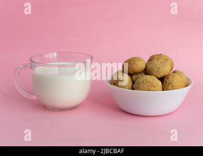 Haferflocken-Kekse auf einem weißen Teller, weiße Milch in transparentem Glas auf einem rosa Hintergrund. Hochwertige Fotos Stockfoto