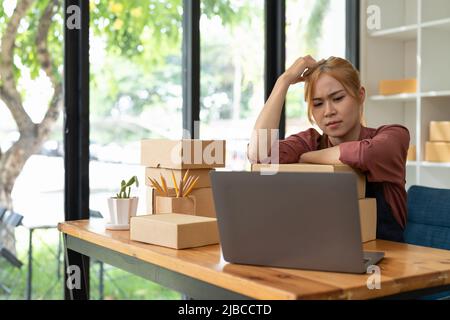 Asiatische Frau denken hart arbeiten Laptop-Computer zu Hause verkaufen online Start-up-Kleinunternehmen Eigentümer, E-Commerce-Ideen-Konzept. Stockfoto