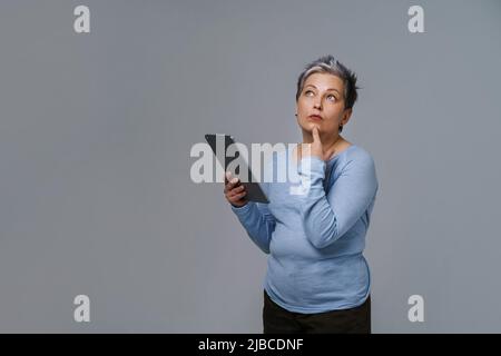 Wunderbare reife Frau 50s grauhaarig mit digitalem Tablet, das in sozialen Medien arbeitet oder überprüft. Hübsche Frau in blauer Bluse isoliert auf weiß. Ältere Menschen und Technologien. Getöntes Bild. Stockfoto