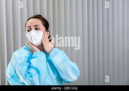 Krankenschwester, die vor dem Besuch des Patienten die Maske N95 auf ihr Gesicht in der Aufnahmestelle justiert Stockfoto