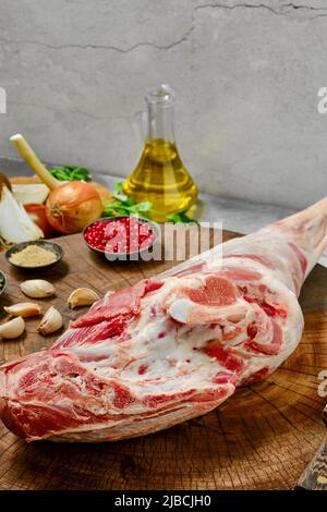 Rohes, ganzes Lammbein-Chump mit Zutaten auf Holzstumpf-Closeup Stockfoto