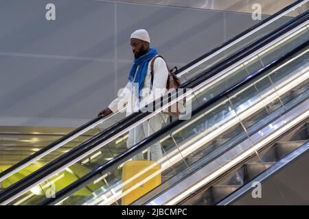 Afroamerikanischer Passagiermann mit Koffer steht auf Rolltreppe, hält Handlauf im Flughafenterminal Stockfoto
