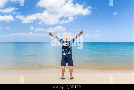 Junger asiatischer Mann hebt die Hände am Meer hoch, Urlaubszeit, glücklicher Urlaub. Stockfoto