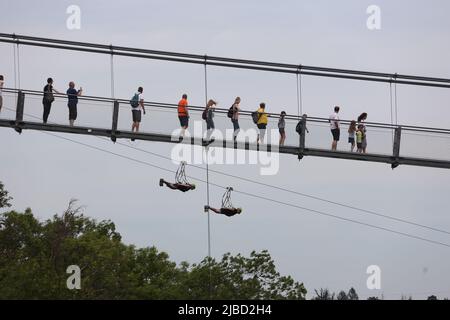 05. Juni 2022, Sachsen-Anhalt, Harz: Besucher wandern über die Hängebrücke am Rappbode-Staudamm, während im Hintergrund zwei Personen mit der Zipline Megazipline fliegen. Am Pfingstwochenende waren die touristischen Ziele im Harz sehr gut besucht. Foto: Matthias Bein/dpa Stockfoto