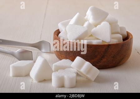 Brückenförmige Zuckerwürfel in Holzschüssel auf weißem Holzhintergrund. Nahaufnahme aus dem unteren Winkel, keine Personen. Stockfoto