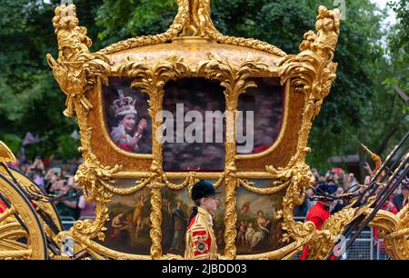 The Mall, London, Großbritannien. 5. Juni 2022. Die Feierlichkeiten zum Platin-Jubiläum der Königin Elizabeth II wurden fortgesetzt, als ein Pageant die Straßen rund um den St. James's Park und den Buckingham Palace besuchte. Die Parade begann in Whitehall und nahm die Mall in Richtung Palast und bestand aus vier Akten, die jeweils verschiedene Aspekte der siebzigjährigen Regierungszeit der Königin darstellten, darunter das Militär aus Großbritannien und dem Commonwealth, historische Referenzen und Prominente. Goldener Staatswagen mit Hologramm von Königin Elizabeth II. Vom Krönungstag, projiziert auf die Fenster Stockfoto