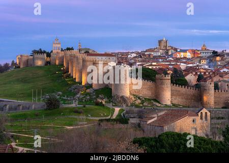 Die Stadtmauern von Avila (Weltkulturerbe der UNESCO) und das Aussichtspunkt Cuatro Postes, das nachts beleuchtet wird. Stockfoto