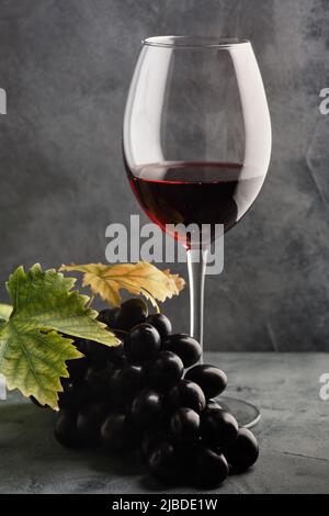 Rotwein im Glas und Trauben auf dem Tisch. Dunkler Hintergrund. Stockfoto