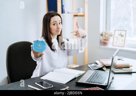 Buchhalter, Geschäftsfrau hält Wecker in den Händen und zeigt auf die Zeit. Stockfoto