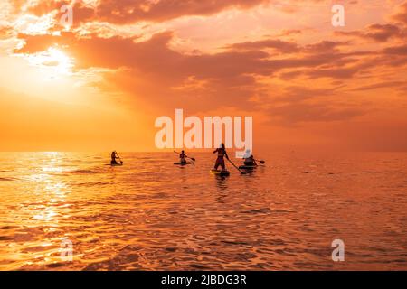 25. Juni 2021. Anapa, Russland. Reisende auf Stand Up Paddle Board am ruhigen Meer mit Sonnenuntergang oder Sonnenaufgang. Gruppe auf Red SUP Boards und Sonnenuntergang mit Wolken Stockfoto