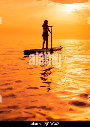 25. Juni 2021. Anapa, Russland. Sportliche Frau auf Stand Up Paddle Board auf See bei Sonnenuntergang oder Sonnenaufgang. Sommertag mit Frau auf Red Paddle-Brett Stockfoto