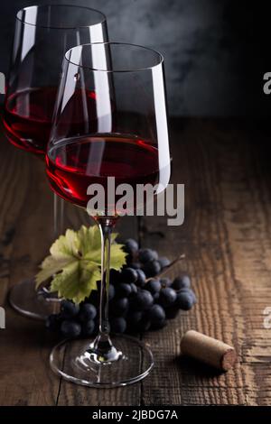 Zwei Gläser Rotwein und ein paar Trauben auf einem alten Holztisch. Dunkler Hintergrund. Stockfoto