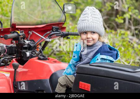 Ein verschmitzter Junge wird mit einem frechen Lächeln und einem Blick zur Seite gesehen. Sitzen auf einem Geländewagen im Wald mit Kopieplatz nach links. Stockfoto