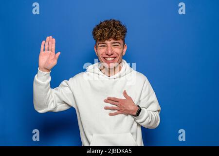 Junger Mann auf blauem Hintergrund isoliert, der einen Eid ablegte und die Hand auf die Brust legte Stockfoto