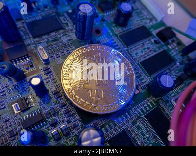 Bitcoin leuchtet ein wenig und reflektiert blaues Licht, die Münze liegt auf der Platine des Computers. Digitale Bitcoin-Technologien. Stockfoto