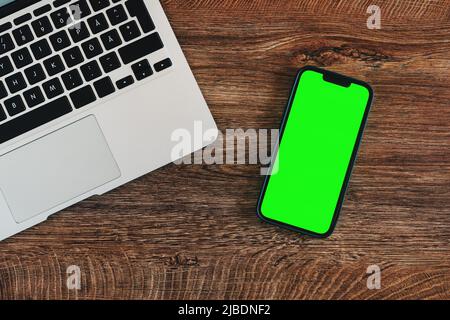 Mobiltelefon mit leerem grünem Mockup-Touchscreen und Laptop-Computer auf dem Büroschreibtisch, Flachbettschlag von oben mit Kopierfläche für Geschäftskommunikation und Stockfoto