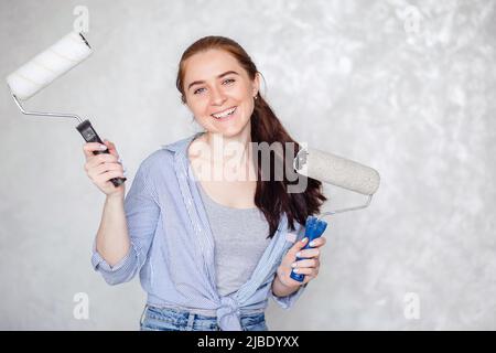 Ein brünett Mädchen ruht sich aus, während es ein Haus repariert. Eine junge lächelnde schöne Frau in legerer Kleidung hält eine Malrolle für ein Wandgemälde Stockfoto