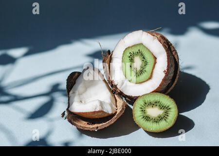 Eine halbe Kokosnuss mit Kiwi und Kokosnussstücken auf blauem Hintergrund. Stockfoto