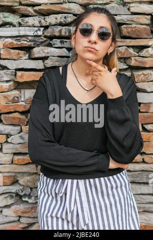 Eine hispanische Dame mit Sonnenbrille sieht nachdenklich aus, während sie ihr Kinn mit ihrer linken Hand berührt Stockfoto