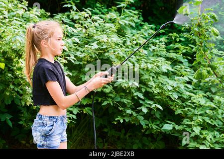 Teenager-Mädchen sprühen ökologische Produkt gegen Blattläuse und andere Schädlinge auf Obstbäume und andere Bäume im Garten und Obstgarten. Selektiver Fokus Stockfoto