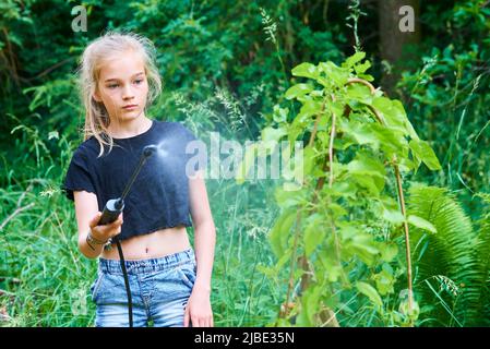 Teenager-Mädchen sprühen ökologische Produkt gegen Blattläuse und andere Schädlinge auf Obstbäume und andere Bäume im Garten und Obstgarten. Selektiver Fokus Stockfoto