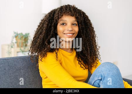 Glückliche junge afroamerikanische Frau, die zu Hause auf der Couch sitzt Stockfoto