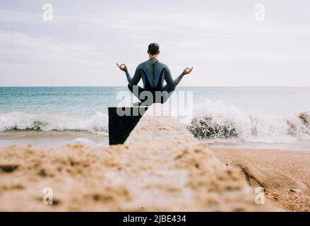 Mann saß meditierend auf einem Strand groyne, bevor er im Meer schwimmen ging Stockfoto